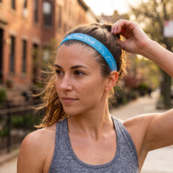 Woman adjusting a blue headband with 'Eat my pixie dust' text, wearing a navy tank top with star patterns.