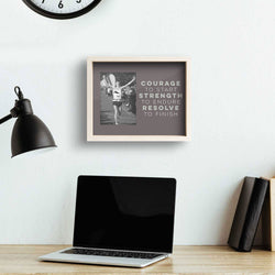 Laptop on a desk with a motivational frame above it, wall clock, and lamp in the background.