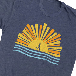 A close-up of a heathered navy blue t-shirt featuring a retro graphic of a running sun over wavy blue lines, with yellow and orange rays.
