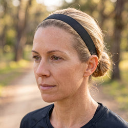 Woman wearing a black headband outdoors with trees in the background