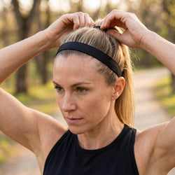Woman adjusting a black headband outdoors with trees in the background