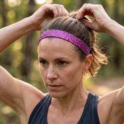 Woman adjusting a purple headband outdoors with a blurred natural background