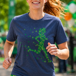 A woman running outdoors wearing a navy blue heathered t-shirt with a green shamrock pattern forming a running figure on the front.