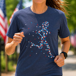 A woman wearing a navy blue t-shirt with a running silhouette made of red, white, and blue stars, photographed outdoors with blurred flags and greenery in the background.