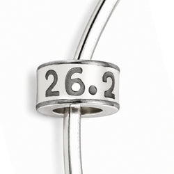 A close-up of a silver charm bead with the engraved numbers '26.2' on a white background.
