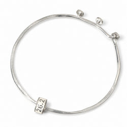 A silver bangle bracelet with a textured finish, featuring a small square charm engraved with '26.2' and a spring-ring clasp closure, shown on a plain white background.