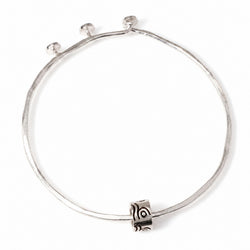 A silver-toned bangle bracelet with a textured, hammered finish, featuring a small cylindrical charm with a spiral pattern and three small bead-like accents along the top curve, shown on a plain white background.