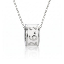 A silver cylindrical pendant necklace engraved with '26.2', suspended from a delicate silver chain against a clean white background with a soft reflection below.