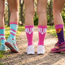 Four pairs of legs wearing colorful socks with 'RUN LIKE GIRL' text on a natural background.