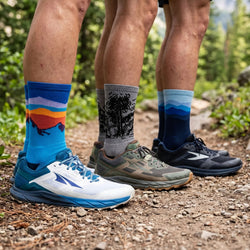 Three pairs of feet wearing colorful socks and running shoes on a trail.