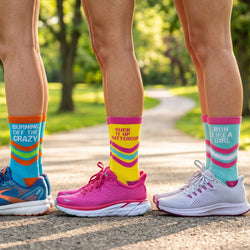 Three pairs of feet wearing colorful socks and running shoes on a path with greenery.
