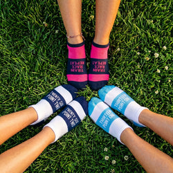 Three pairs of feet wearing colorful socks with text on grass