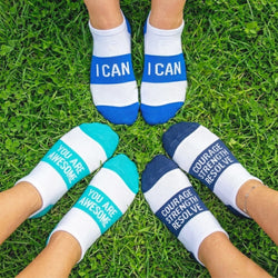 Three pairs of feet wearing socks with motivational text on a grass background