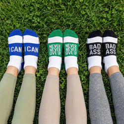 Three pairs of socks with motivational text on a grassy field