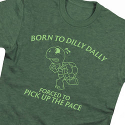 A close-up of a heather green t-shirt featuring a light green graphic of a turtle and the text 'BORN TO DILLY DAILY' and 'FORCED TO PICK UP THE PACE'.