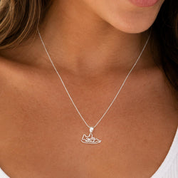 A close-up of a woman wearing a delicate silver chain necklace with a small shoe-shaped pendant featuring '26.2' cut out in the center.
