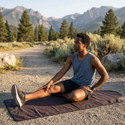 Man stretching outdoors on a mat with mountains in the background