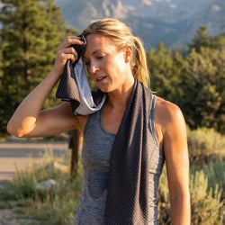 Woman in a sleeveless top with a towel draped over her shoulder outdoors.