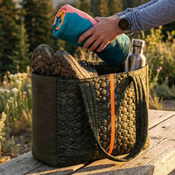 Person packing a quilted bag with hiking boots and a water bottle outdoors.