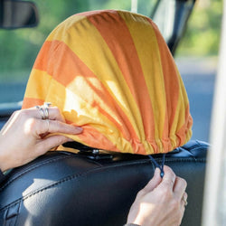Person adjusting a yellow and orange seat cover on a car seat.