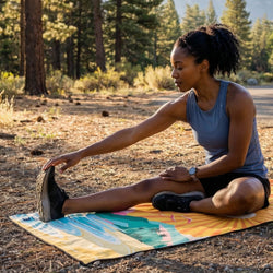 Woman stretching on a colorful mat in a forest setting