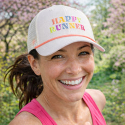 Woman wearing a 'Happy Runner' cap with a blurred natural background
