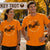 A man and a woman wearing matching bright orange graphic t-shirts with a turkey illustration and the words 'Run Now, Gobble Later' in an outdoor autumn setting.