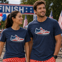 A man and a woman standing outdoors in matching navy blue t-shirts with a red, white, and blue running shoe graphic.