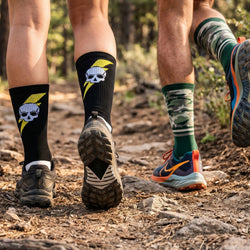Two pairs of socks with skull and camo design on a trail.
