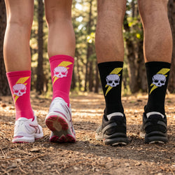 Two pairs of legs wearing socks with skull designs in a forest setting.