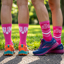 Two pairs of legs wearing pink socks with text and colorful running shoes on a grassy background.
