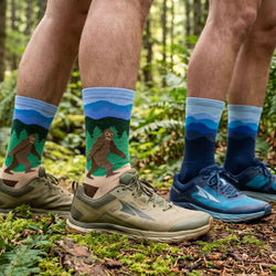 Two pairs of feet wearing socks with nature-themed designs in a forest setting.