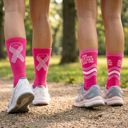 Pink socks with breast cancer awareness ribbons worn outdoors on a path.