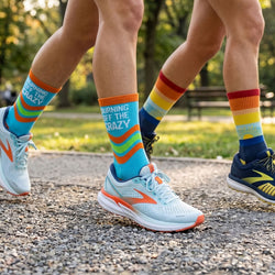 Two pairs of legs wearing colorful socks and running shoes on a path with greenery in the background.