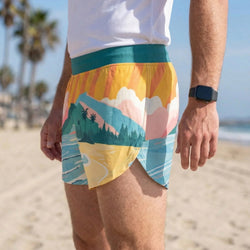 Person wearing colorful beach shorts with a scenic design on a beach.