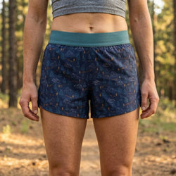 Person wearing blue mountain patterned shorts with a green waistband in a forest setting