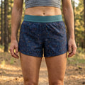 Person wearing blue mountain patterned shorts with a green waistband in a forest setting