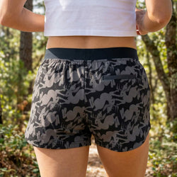 Person wearing black and gray jackalope patterned running shorts with a white top in a forest setting