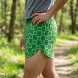 Person wearing green checkered shorts with shamrock pattern in a forest setting