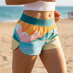 Person wearing colorful beach-themed shorts on a sandy beach with ocean in the background
