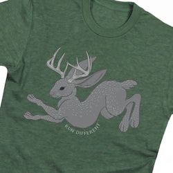 A close-up of a heather green t-shirt featuring a gray graphic of a jackalope with antlers and the text 'RUN DIFFERENT' printed below it.
