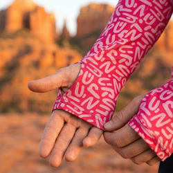 Close-up of hands wearing pink patterned sleeves showing a thumbhole against a blurred natural background