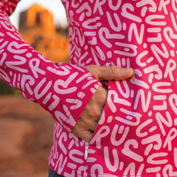 Person wearing a pink jacket with white text pattern showing zippered side pocket blurred outdoor background