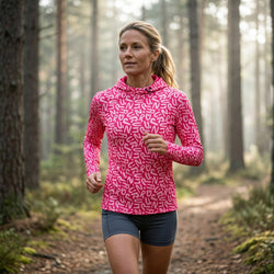 Woman running in a forest wearing a pink patterned running hoodie.