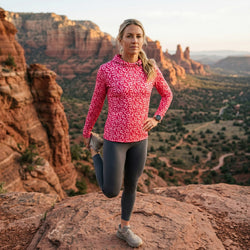 Woman in pink running hoodie stretching on a rocky outcrop with desert landscape in the background