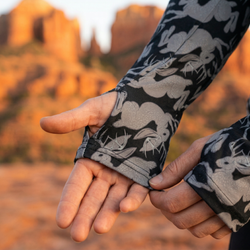 Close-up of hands wearing jackolope patterned jacket showing thumbhole feature with a desert landscape in the background