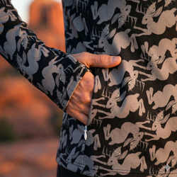 Close-up of a person wearing a black jacket with a jackalope pattern showing the zippered side pocket, blurred natural background