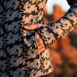 Person wearing a jacket with a jackalope pattern showing a zippered side pocket in a natural setting