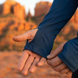 Person adjusting a blue sleeve showing a thumbhole in a desert landscape with warm colors