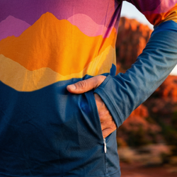 Person wearing a blue jacket with a colorful mountain design showing a zippered side pocket.
